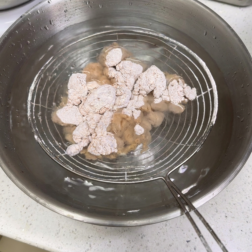 Poulet fariné immergé dans un bol deau à laide dune écumoire.