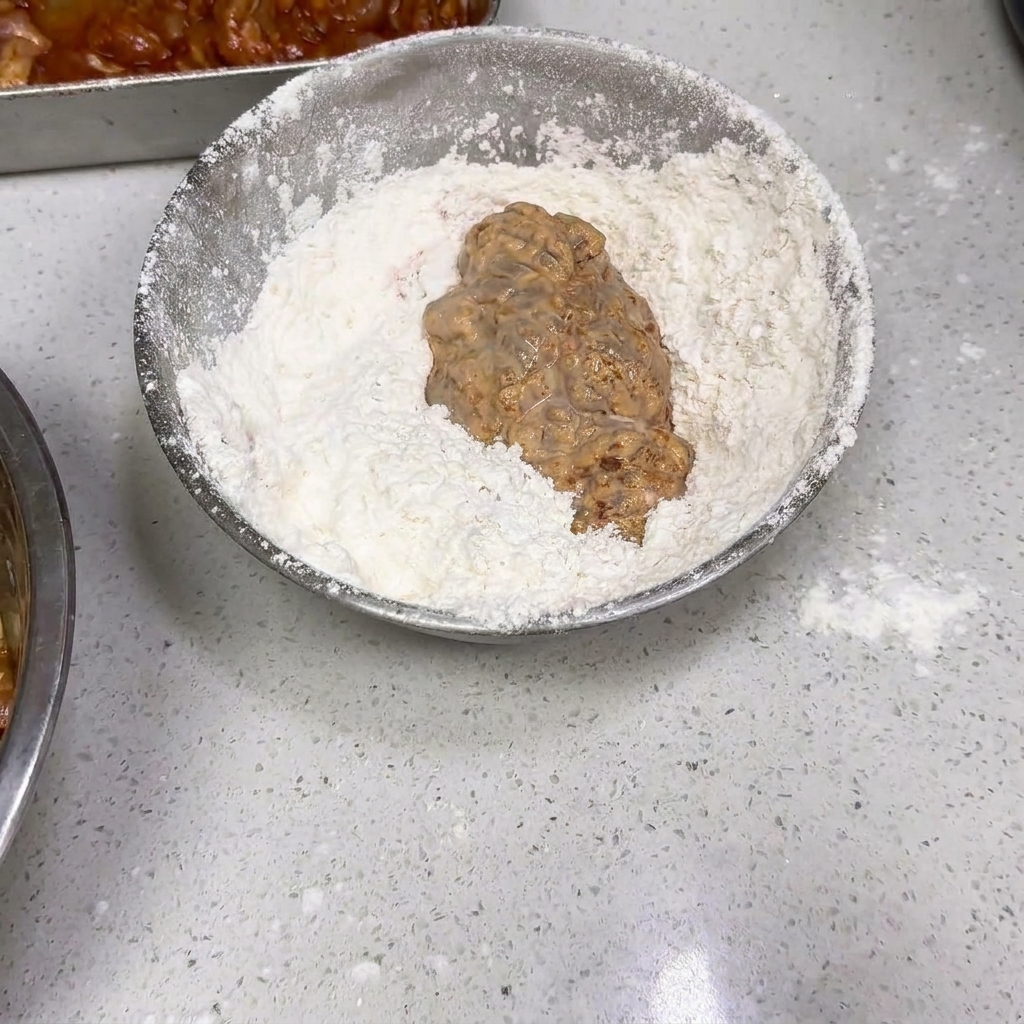 Poulet mouillé mélangé dans un bol de farine sèche.