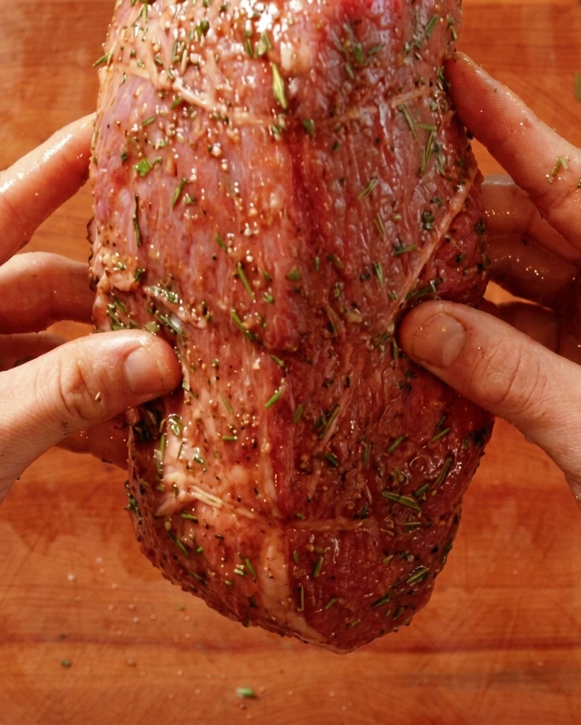 Mains plaçant un rôti de bœuf cru assaisonné dans une poêle chaude.