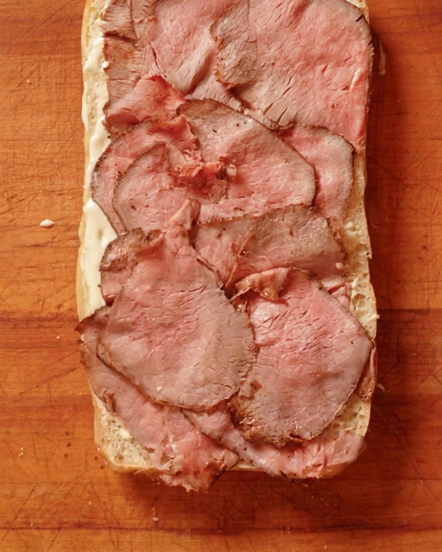 Tranches fines de roast beef cuit disposées sur une couche de sauce sur le pain.