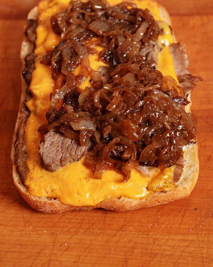 Oignons caramélisés riches et sombres déposés sur le cheddar.