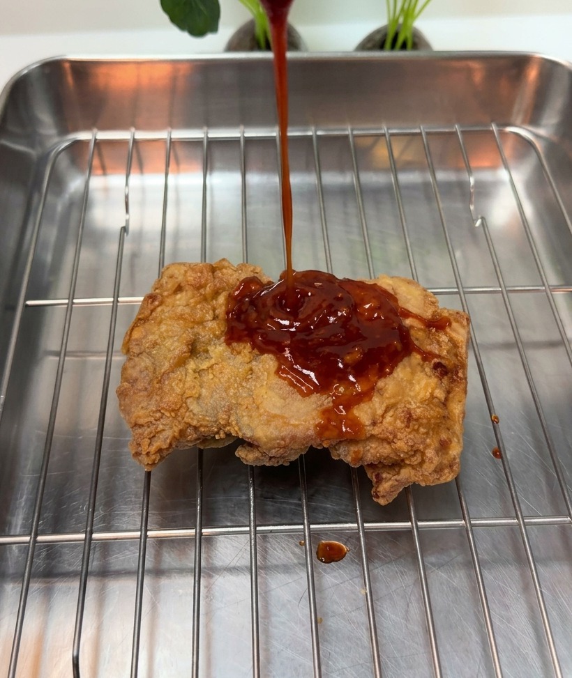 Une sauce rouge épaisse versée sur un morceau de poulet frit croustillant posé sur une grille métallique.