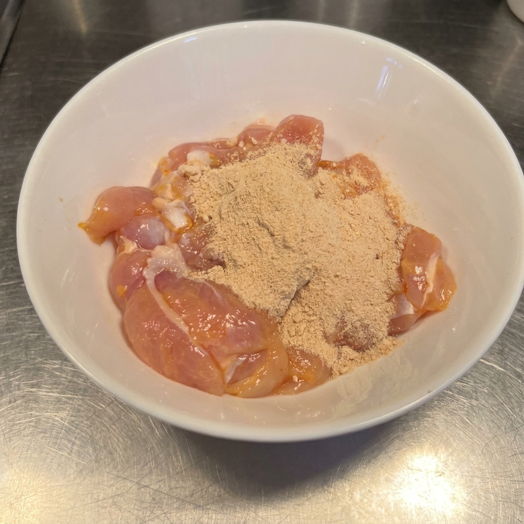 Cuisses de poulet crues dans un bol, enrobées dun mélange dépices rouge-brun.
