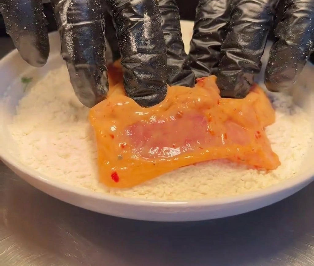 Une cuisse de poulet marinée déposée dans une assiette de farine.