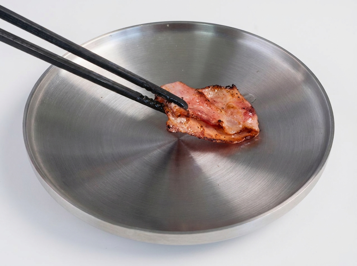 Une spatule retournant un steak haché bien doré dans une poêle brûlante.