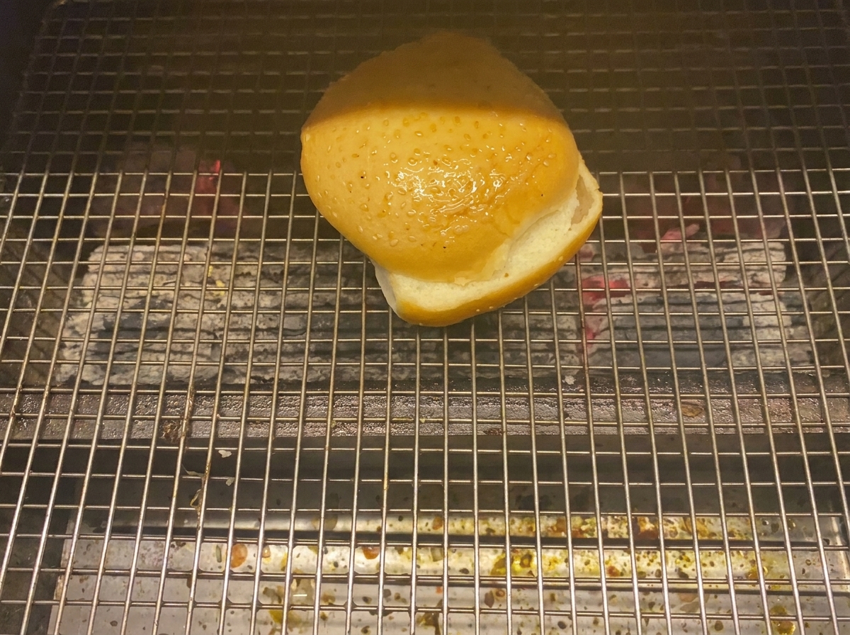 Une moitié de pain à burger toastant face contre grille sur un barbecue.