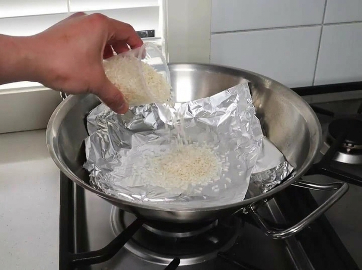 Riz cru et copeaux de bois répartis sur du papier aluminium dans un wok.