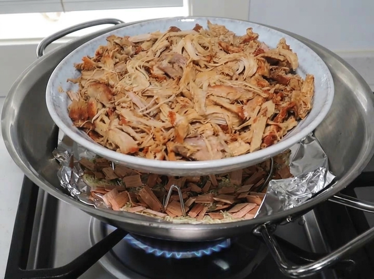 Assiette de porc effiloché sur une grille à lintérieur du wok au-dessus du mélange de fumage.