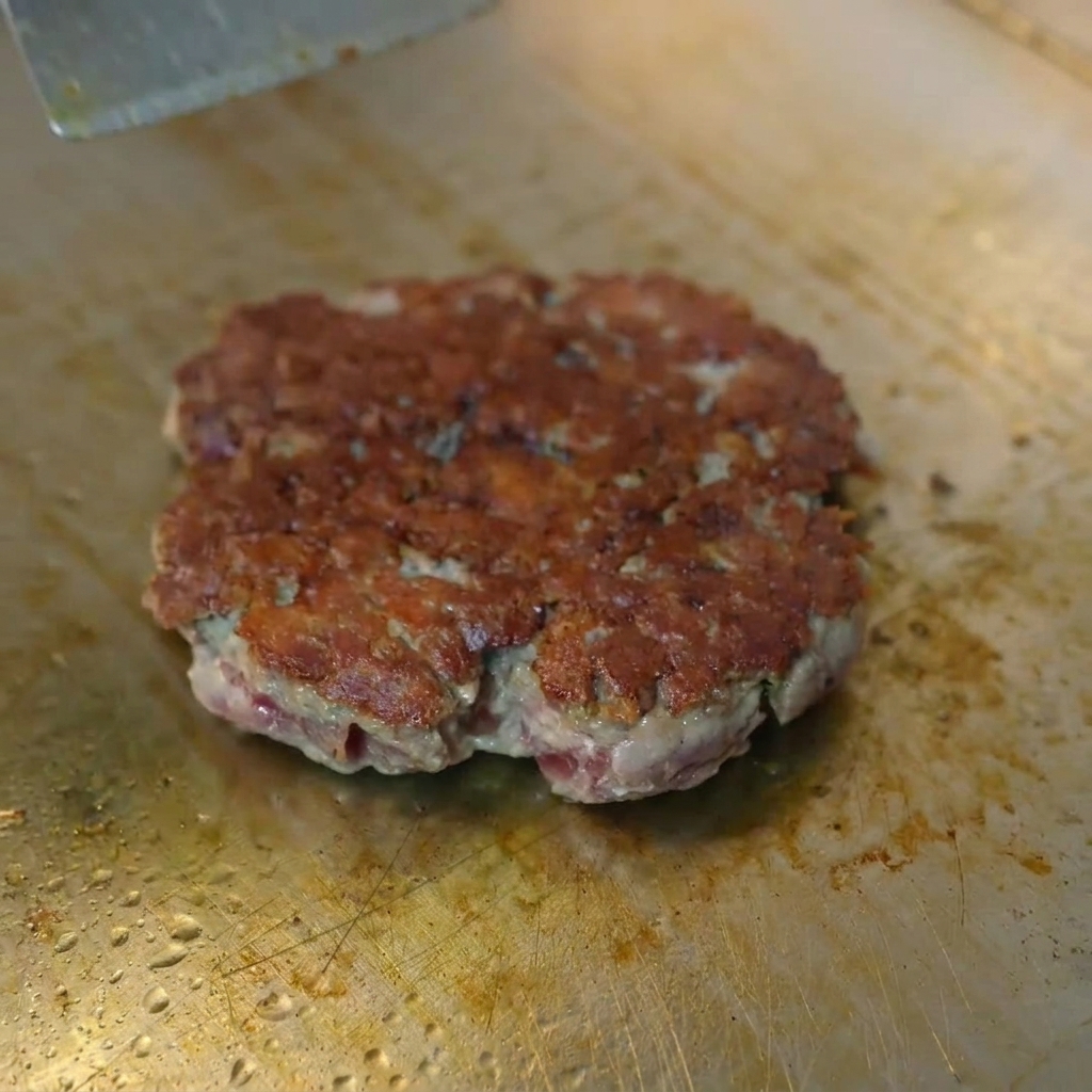 Une tranche de fromage jaune fondant sur un steak bien doré sous une cloche de cuisson en métal.