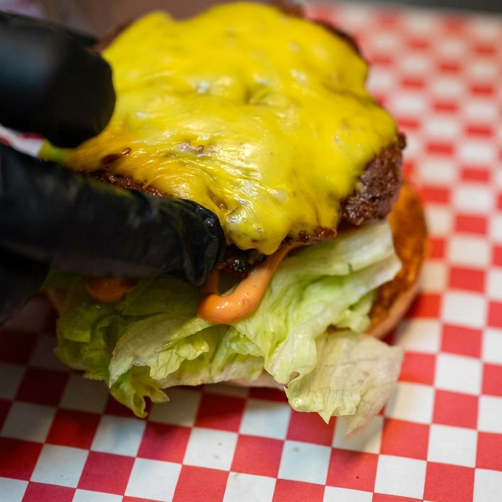Le steak haché recouvert de fromage fondu déposé sur le lit de laitue et de tomate.
