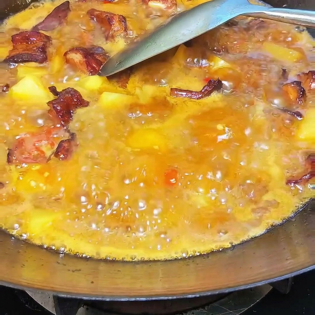 Une cuillerée de saindoux crémeux mélangée au ragoût bouillonnant dans un wok.