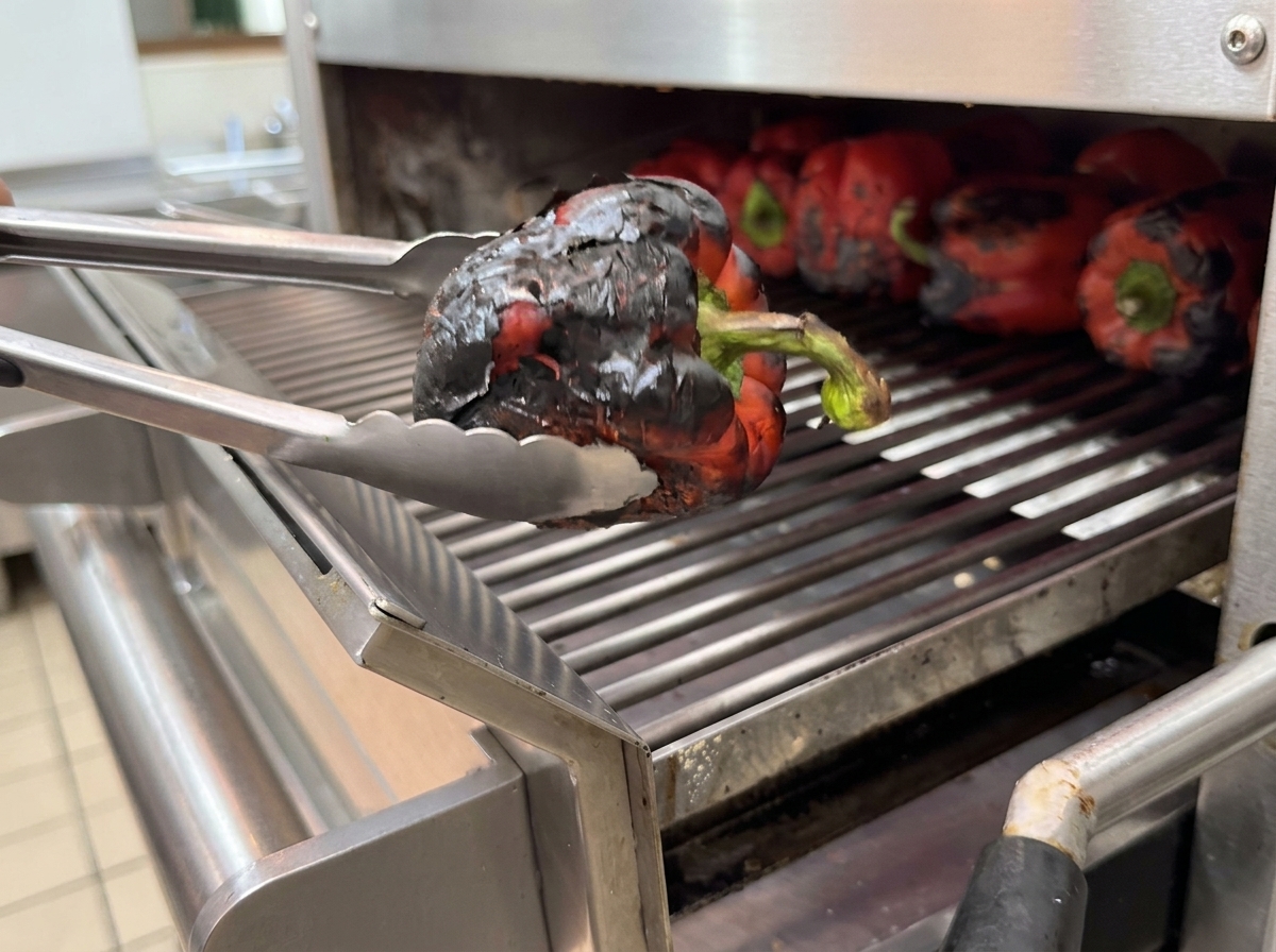 Poivrons grillés dans un récipient recouvert de film plastique pour laisser vapeur.
