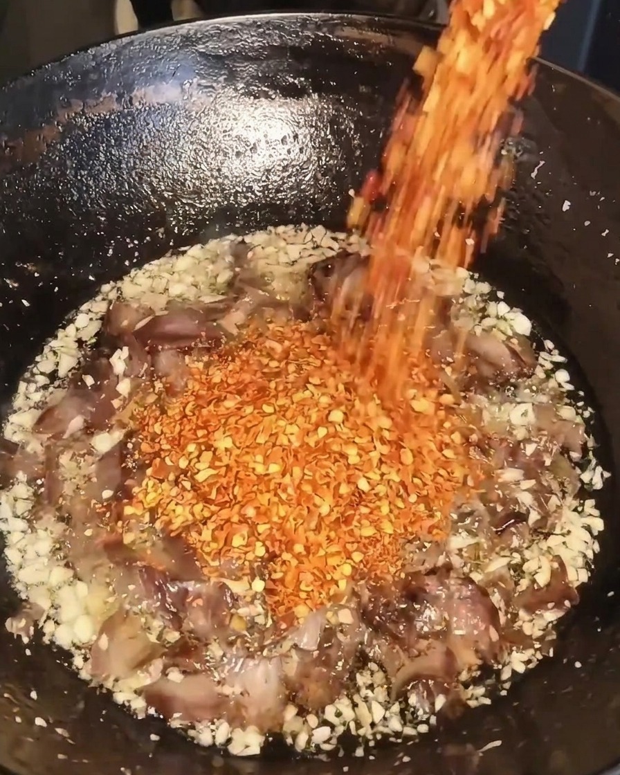 Flocons de piment rouge versés dans le wok contenant lail, le bœuf et lhuile.