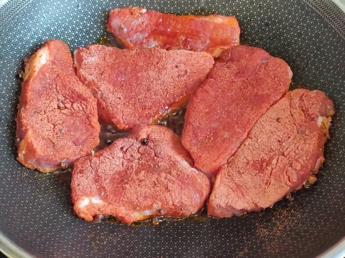 Des morceaux de porc assaisonnés en train de dorer dans une poêle chaude.