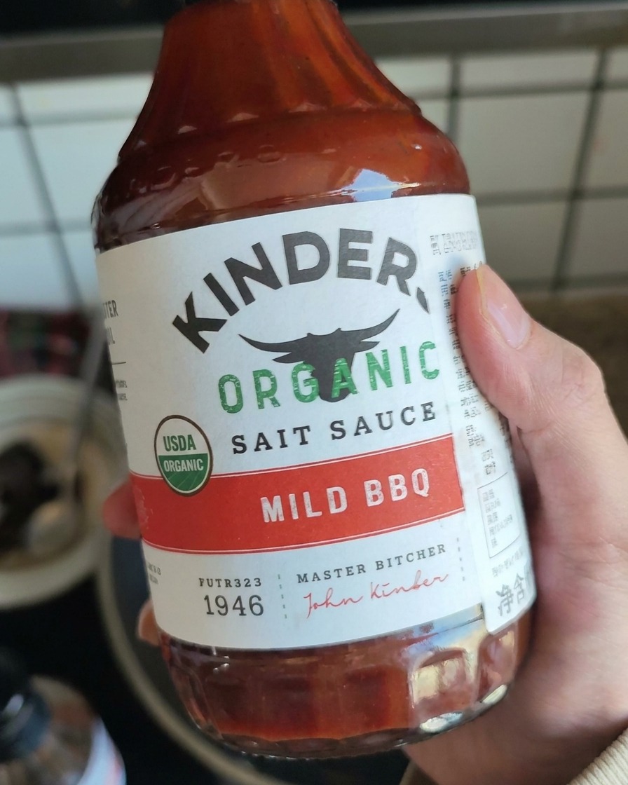 Une main tenant une bouteille de sauce BBQ douce prête à être versée sur la viande.