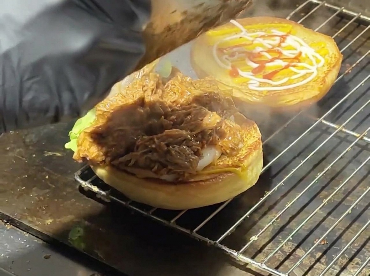 Porc effiloché à la sauce déposé sur un pain grillé avec de la laitue sur une plaque de cuisson.