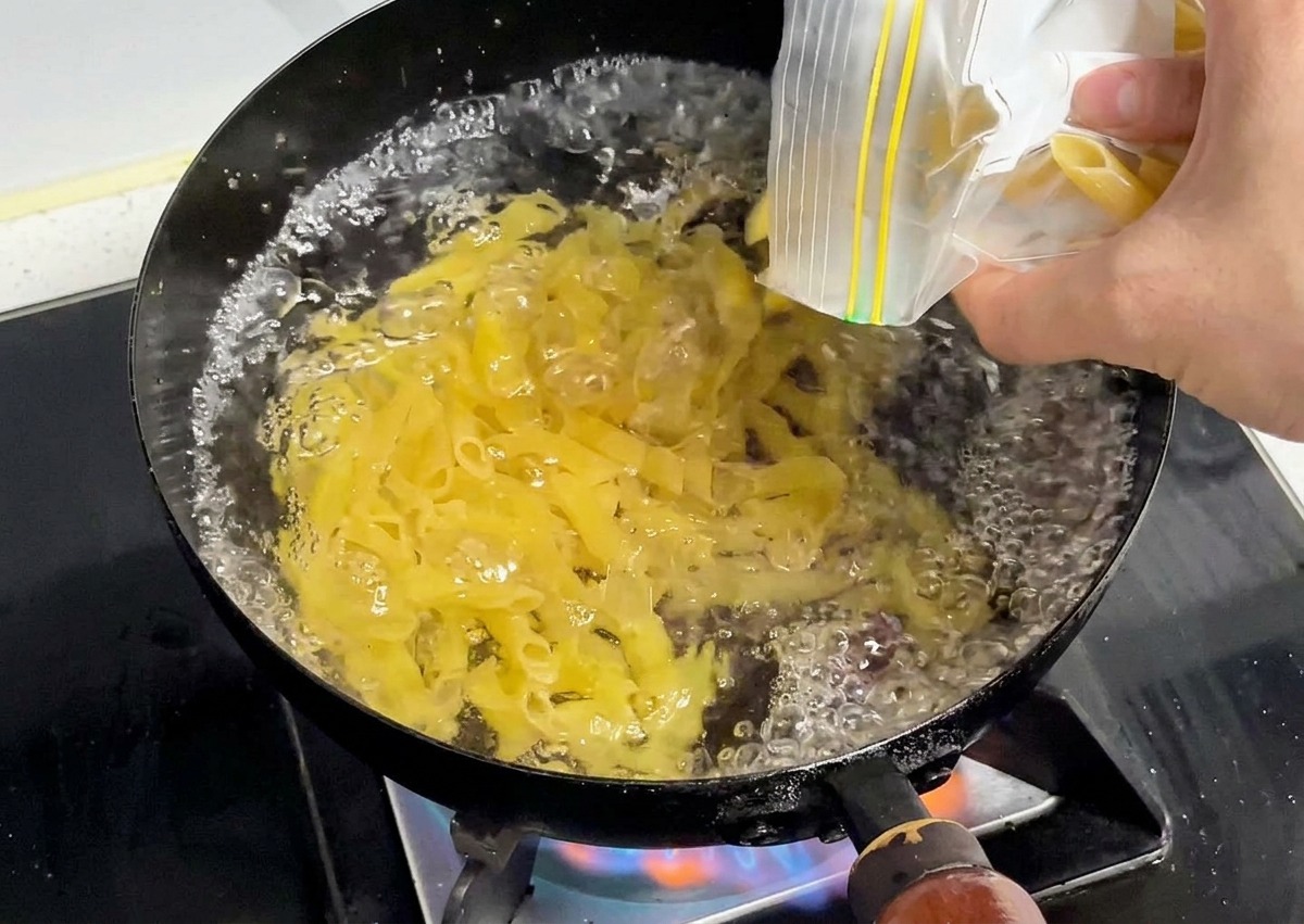 Penne sèches versées dans une marmite deau en pleine ébullition.