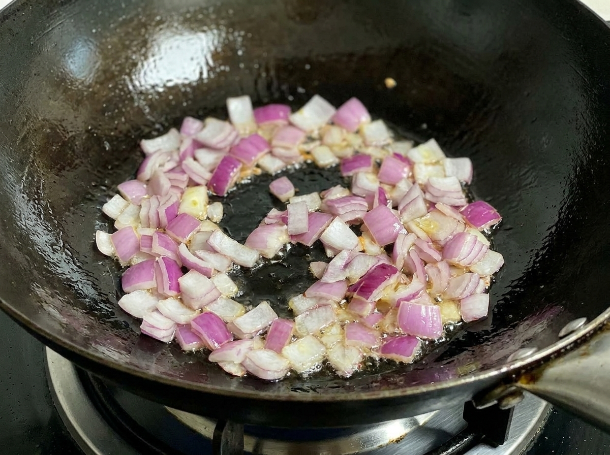 Oignons rouges hachés frits dans un wok chaud avec de lhuile, remués par une spatule noire.