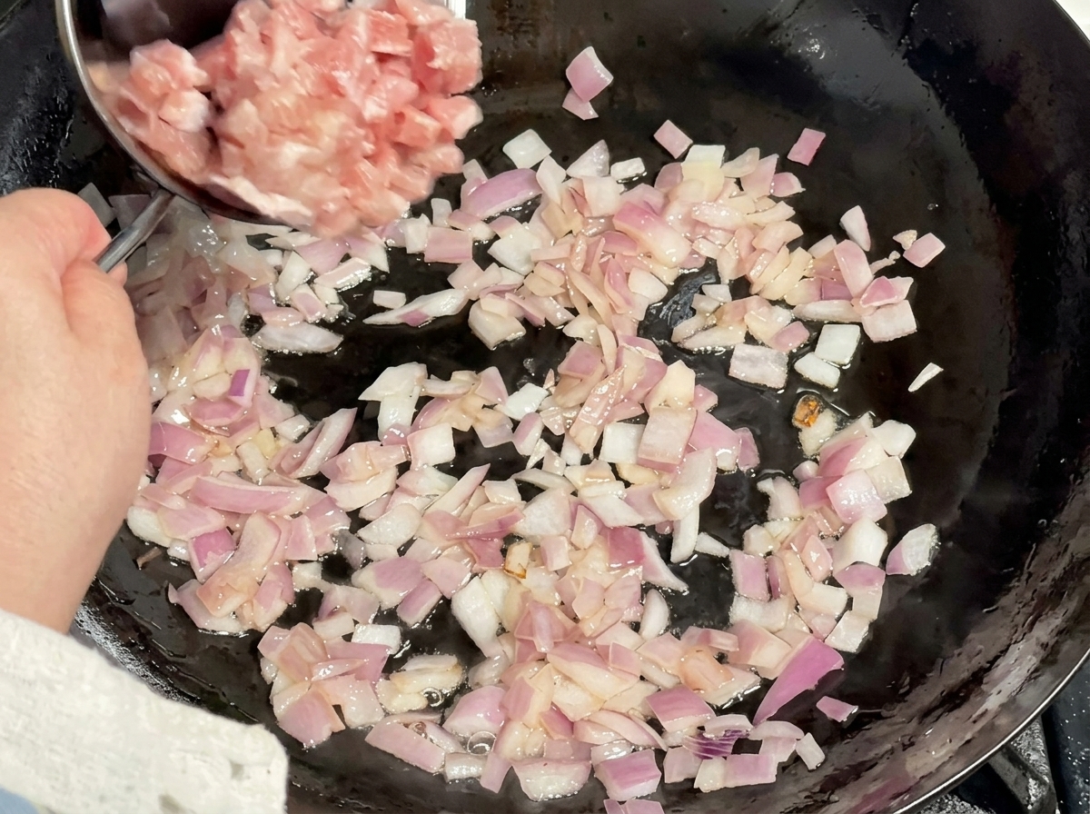 Porc cru en cubes versé dun bol en métal dans un wok rempli doignons rouges revenus.