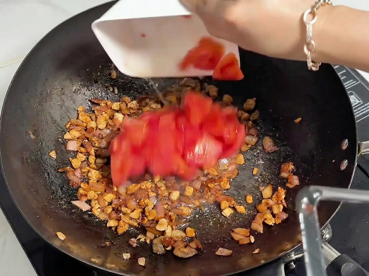 Tomates rouges fraîches hachées ajoutées dun bol blanc dans un wok contenant la viande hachée cuite.