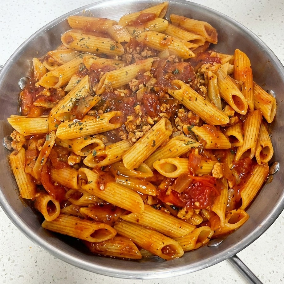 Gros plan dune poêle de macaroni à la sauce viande tomate garnie dune tranche de fromage et dherbes séchées saupoudrées.