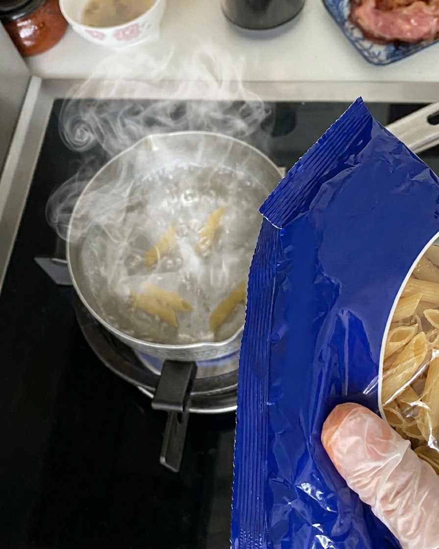 Des penne sèches versées dun emballage bleu dans une casserole deau bouillante.