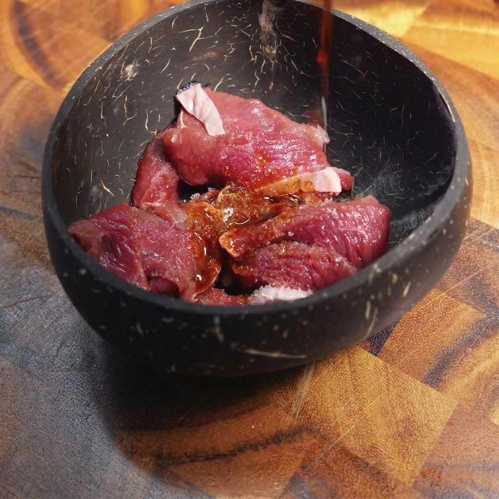 Sauce marinade foncée versée sur du bœuf cru finement tranché dans un bol.