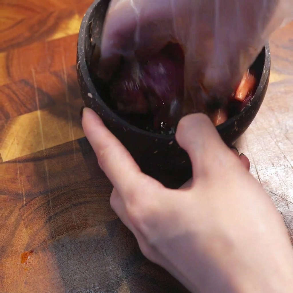 Une main gantée mélange le bœuf cru tranché avec les assaisonnements sombres dans un bol.