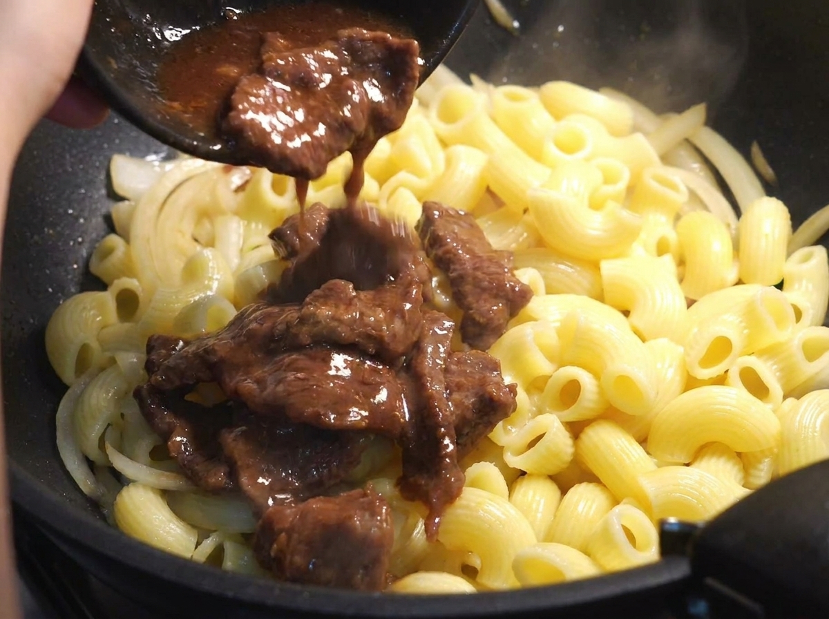 Tranches de bœuf partiellement cuites avec marinade ajoutées dans une poêle avec macaronis et oignons.