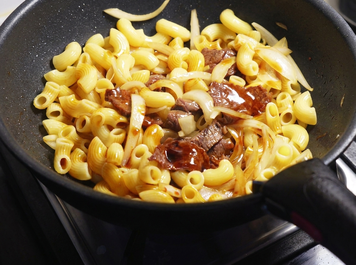 Sauce soja foncée versée sur des macaronis, des tranches de bœuf et des oignons dans une poêle noire.