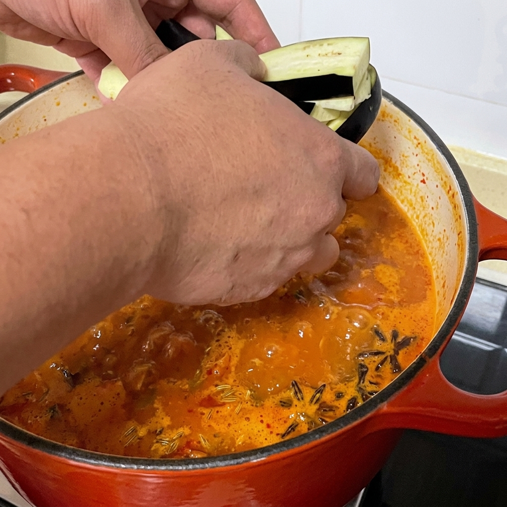 Lanières daubergine tranchées ajoutées dans la marmite de soupe de palourdes épicée.