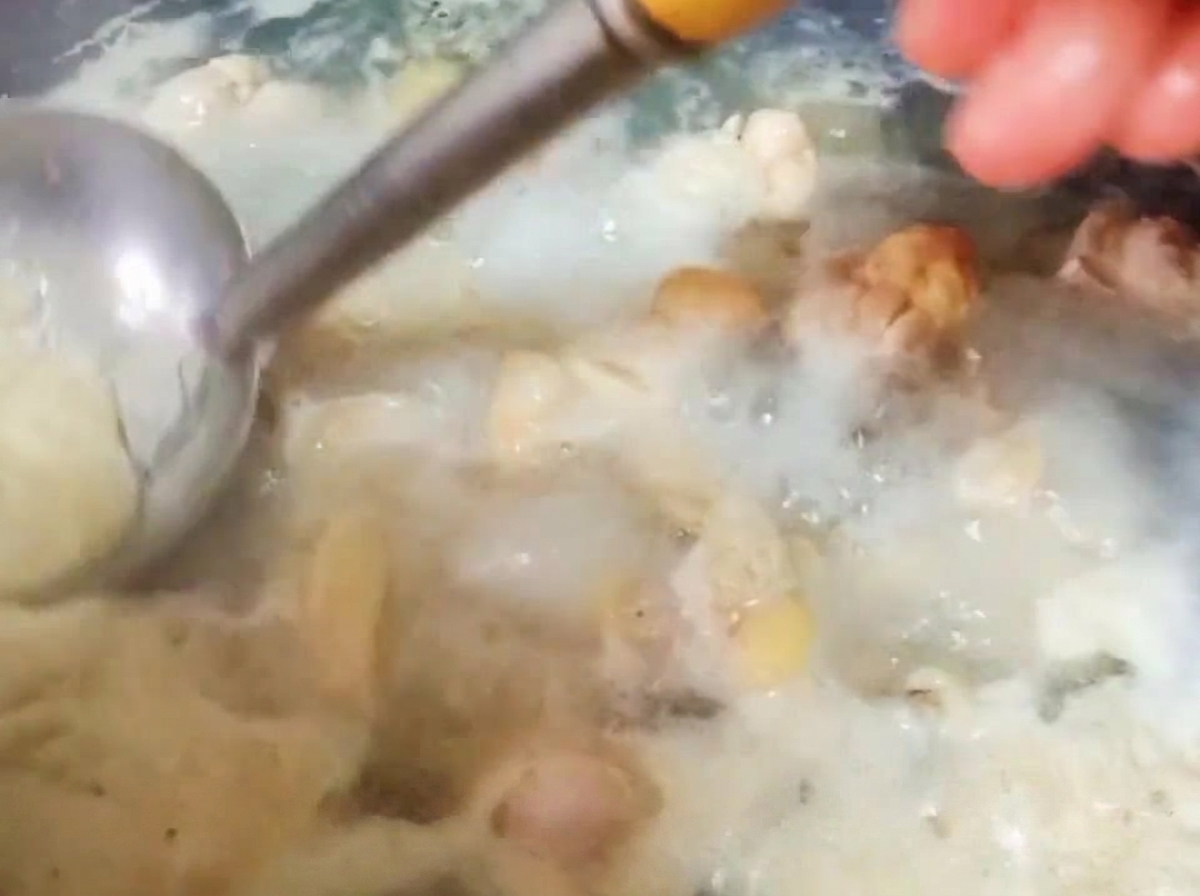 Une louche en métal retirant la mousse épaisse à la surface de leau bouillante contenant les morceaux de poulet.