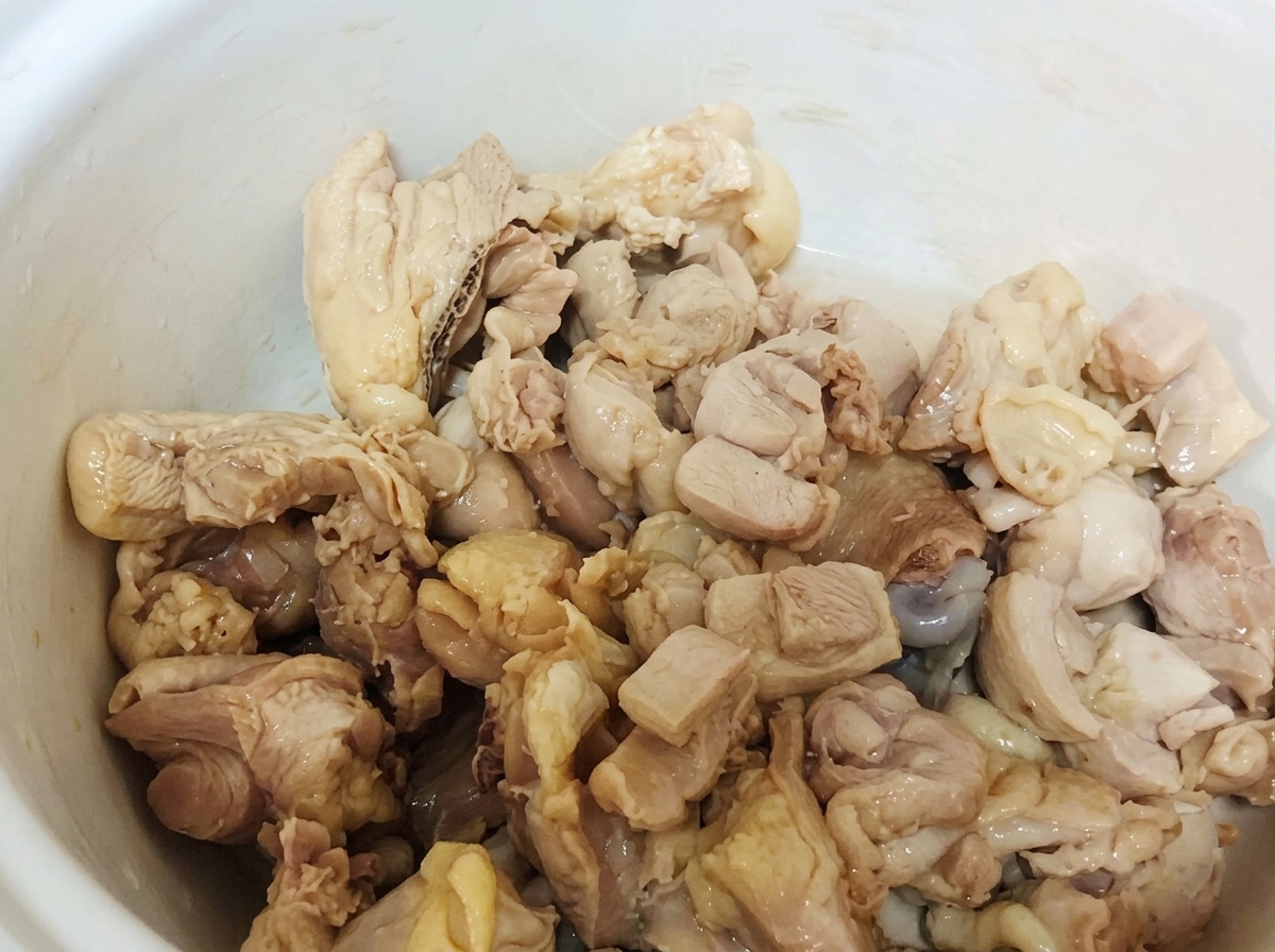 Morceaux de poulet blanchis reposant au fond dune marmite en céramique blanche.