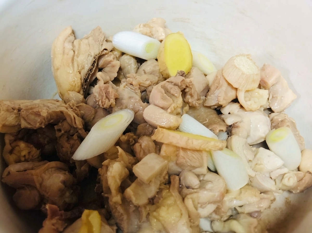 Morceaux de poulet dans une marmite en terre cuite assaisonnés avec des oignons verts, du gingembre et des sauces.