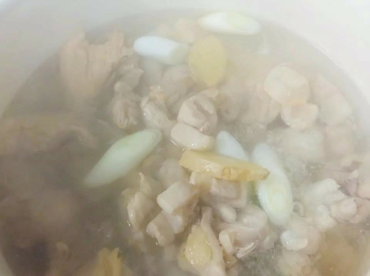 Eau très chaude versée dans une marmite blanche sur les morceaux de poulet, le gingembre émincé et la cébette.
