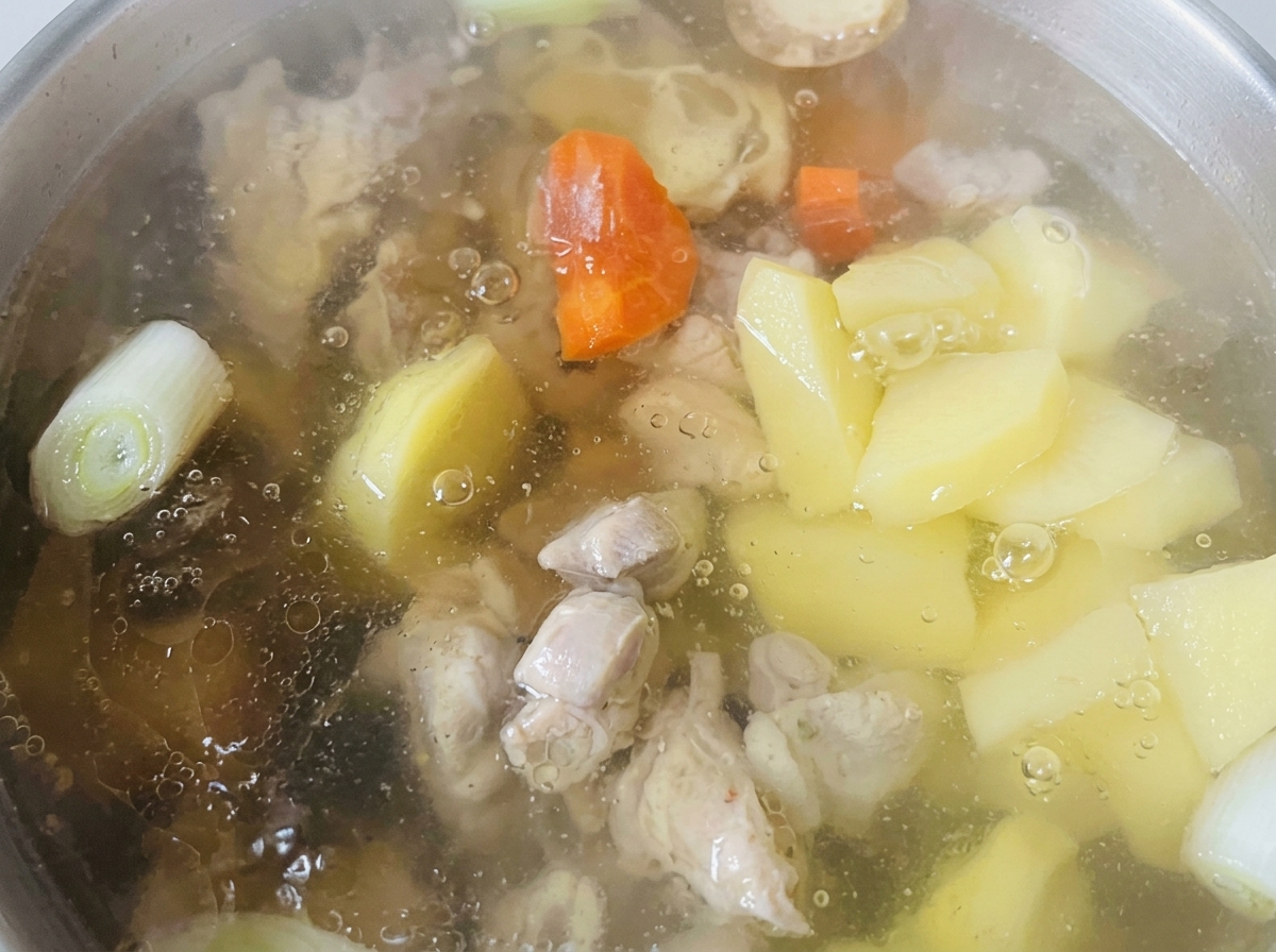 Morceaux de carottes et de pommes de terre cuisant dans un bouillon clair aux côtés du poulet.
