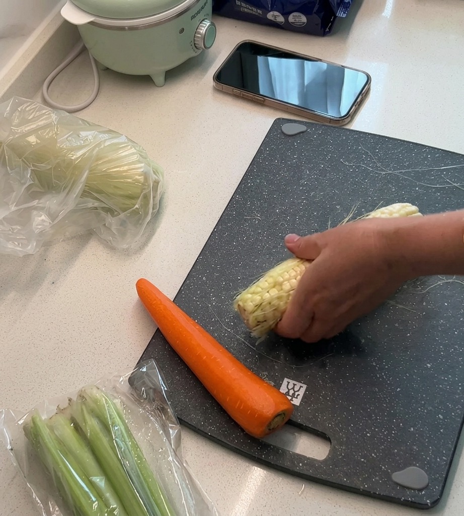 Des grains de maïs frais tranchés sur une planche à découper, avec les feuilles et les barbes mises de côté.
