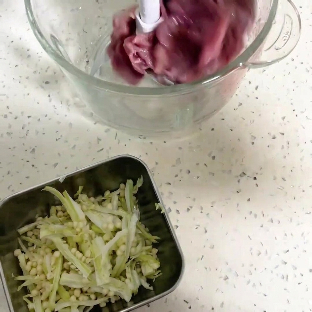 Gros plan sur un bol de robot culinaire contenant des morceaux de viande de canard rouge sombre et des graines de gombo.