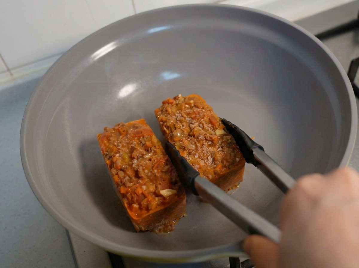 Des blocs congelés de pâtes et de sauce à la viande chauffés dans une poêle à laide de pinces.