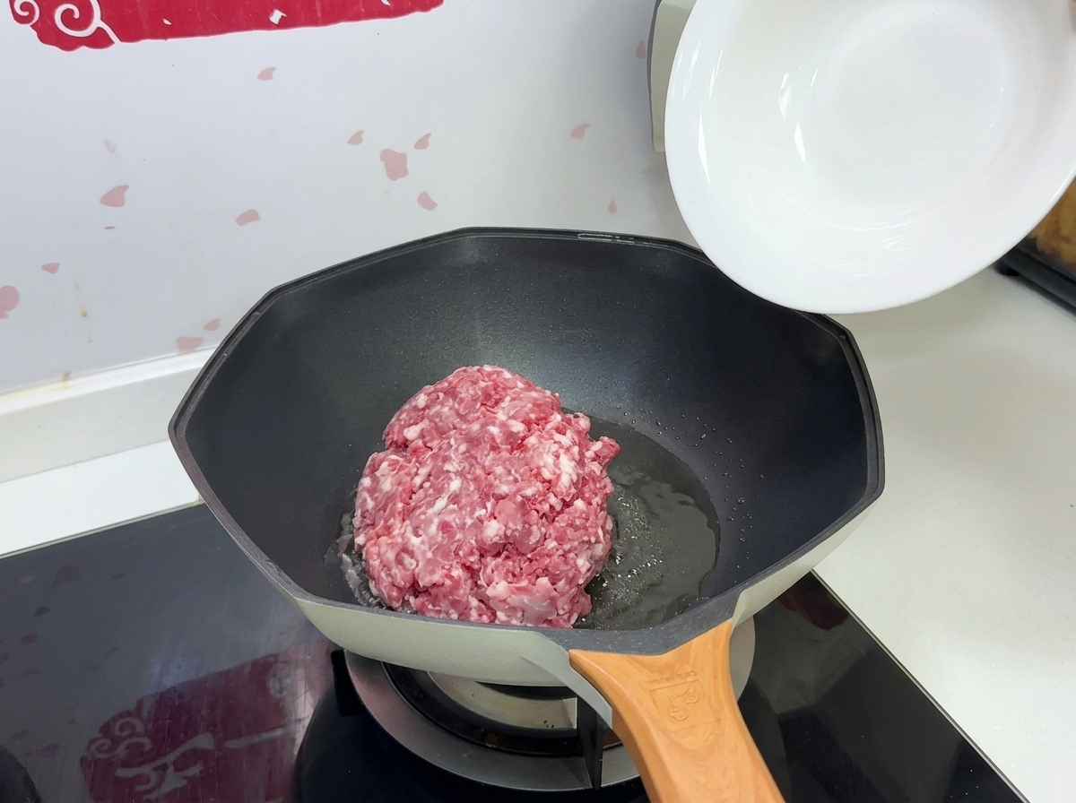 Une portion de porc haché cru versée dun bol blanc dans une poêle chaude avec de lhuile.