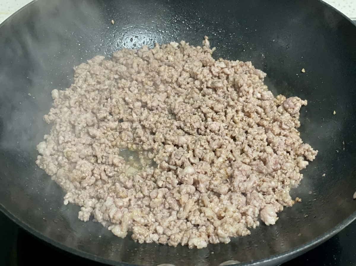 Miettes de porc haché cuites et légèrement dorées grésillant dans un wok sombre.