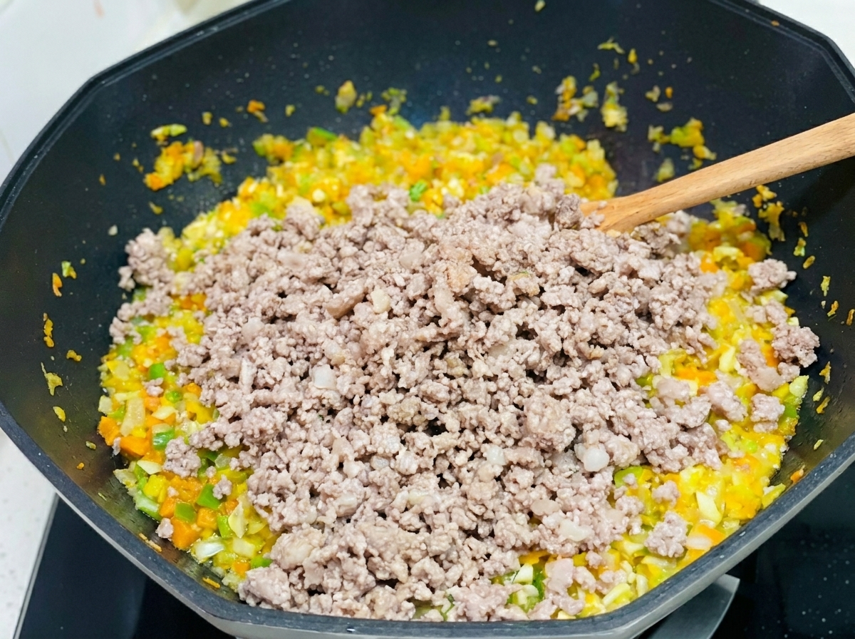 Porc haché incorporé à un mélange de carottes, céleri et oignons sautés dans un grand wok.