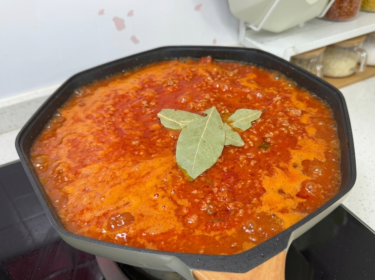Sauce tomate à la viande mijotant dans un wok, assaisonnée de sel, sucre, laurier et poivre.