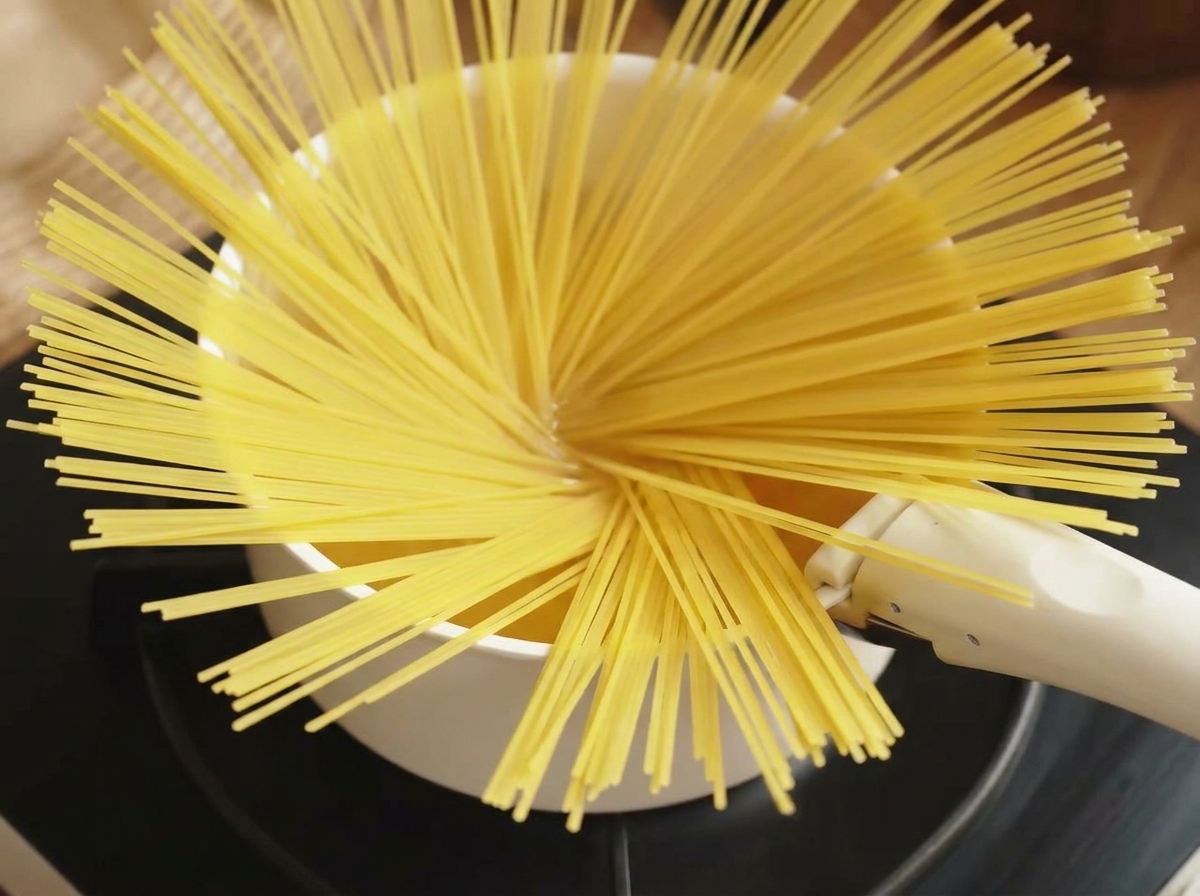 Poignée de spaghettis secs jetée dans une marmite deau bouillante.