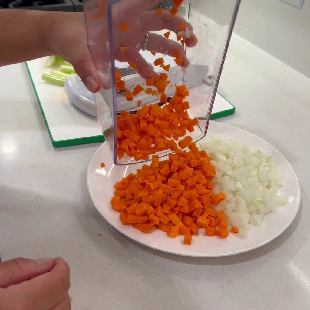 Des carottes en dés déposées par un hachoir transparent sur une assiette avec des oignons.