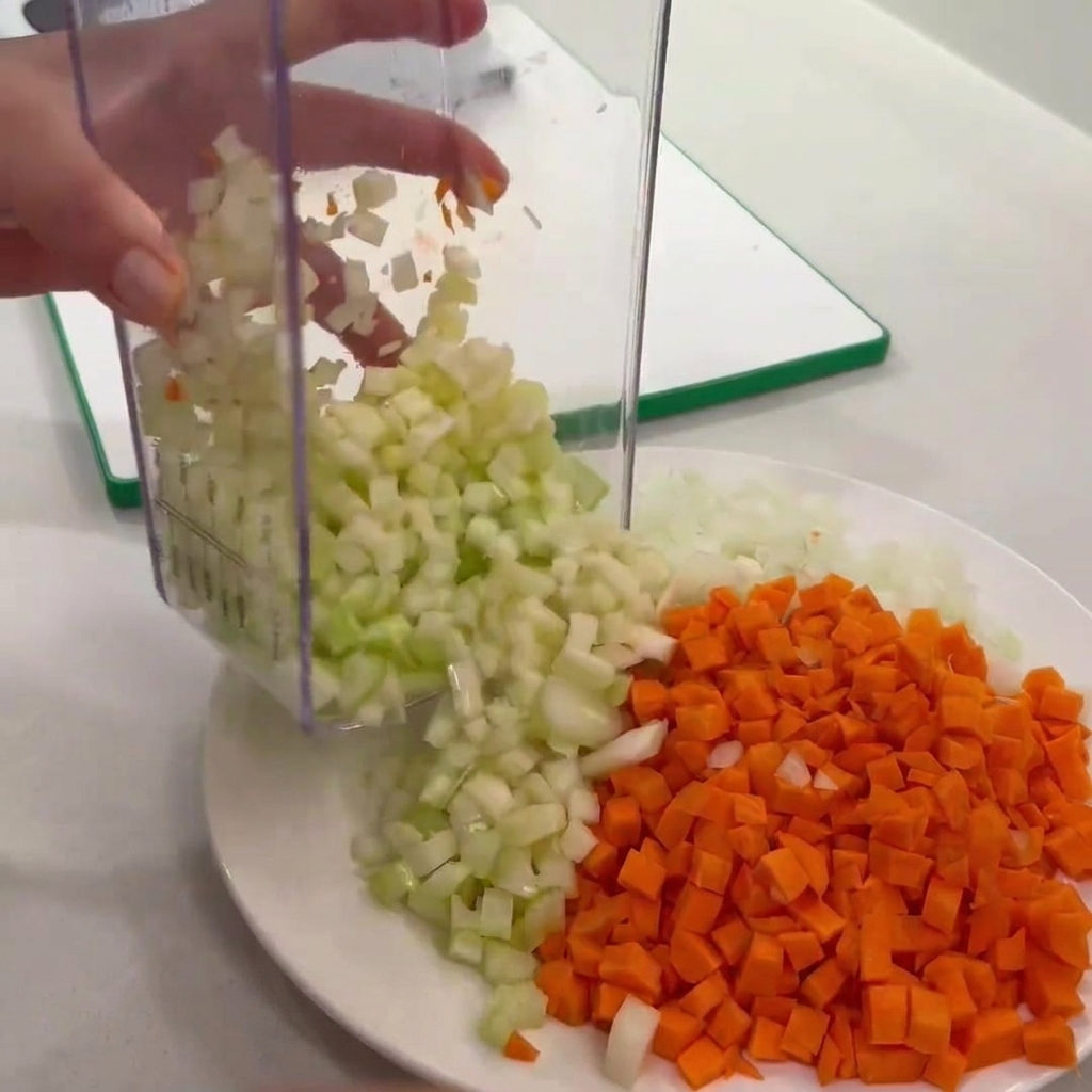 Du céleri en dés vidé dun hachoir sur une assiette à côté des carottes et oignons.