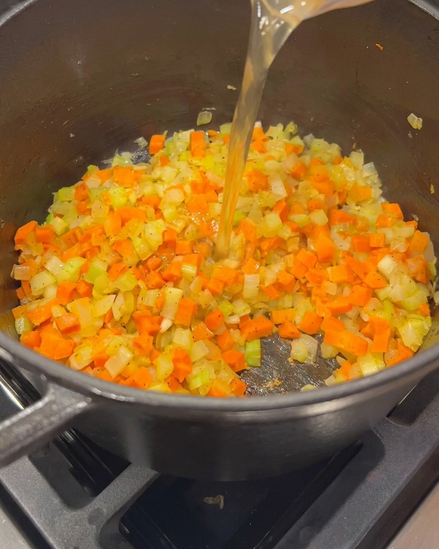 Du bouillon de volaille doré versé dun verre doseur dans une marmite contenant les légumes revenus.
