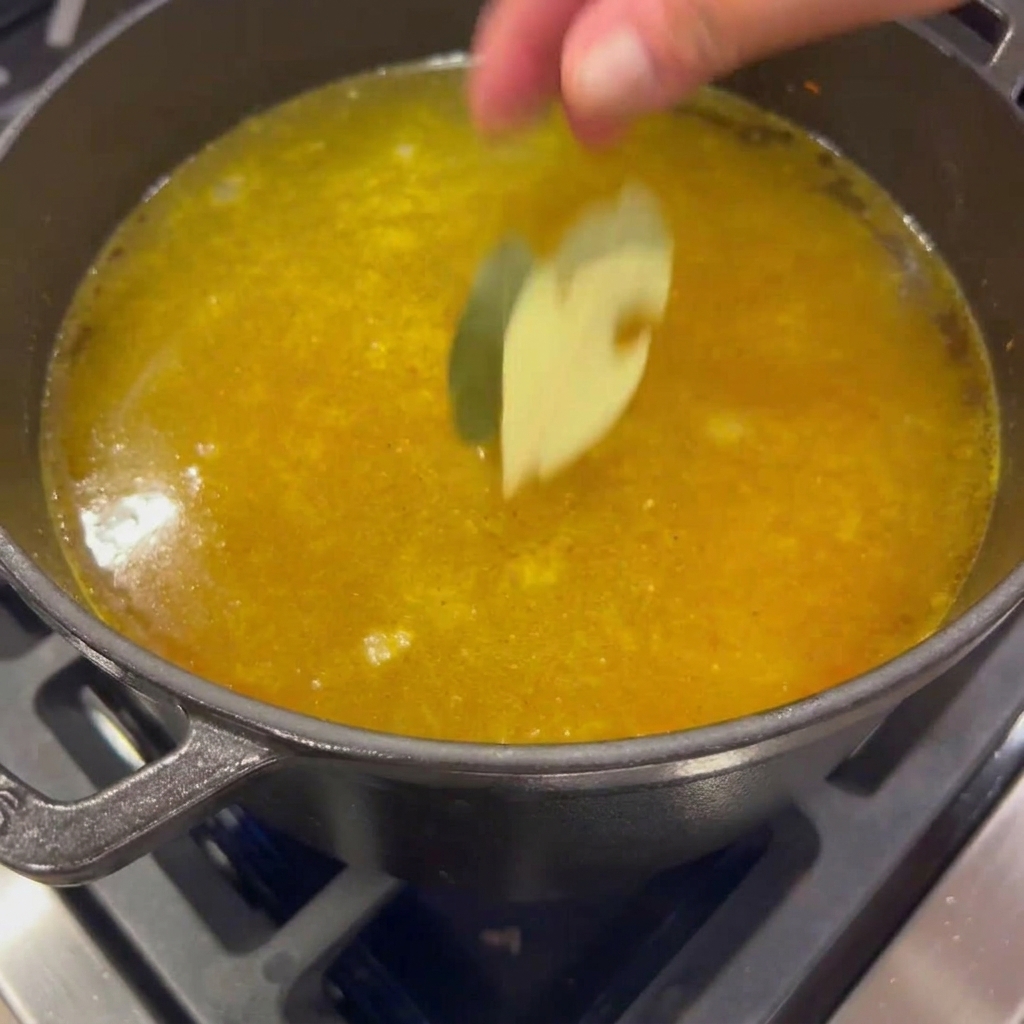 Deux feuilles de laurier séchées tombant dans une marmite de bouillon doré et frémissant.