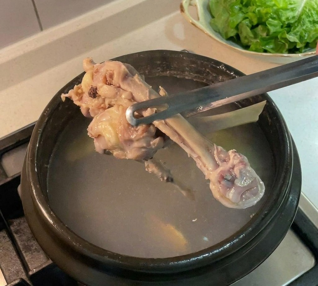 Os de poulet retirés dune marmite sombre avec des pinces.