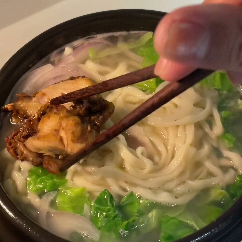 Morceaux de poulet rôti déposés sur les nouilles dans le bol.